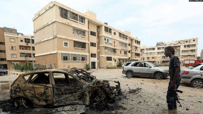 Un combattant loyal au gouvernement d'entente nationale (GNA) reconnu par l'ONU en Libye se tient à côté d'une voiture détruite suite à un bombardement à Tripoli, le 9 mai 2020.